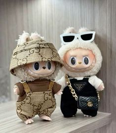 two stuffed animals wearing clothes and sunglasses on top of a wooden shelf next to each other