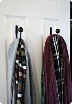 two coats hanging on hooks in front of a white door with plaid scarfs and scarves