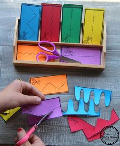 a person cutting out paper with scissors on a wooden table next to some cut outs