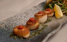 three sea scallops on a plate with garnish and lemon wedges