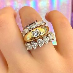 a woman's hand holding two rings with diamonds on them and the middle one has a heart shaped diamond in it