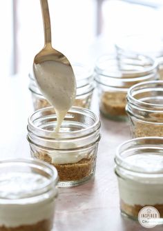 a spoon is being drizzled over some food in small glass jars on a table