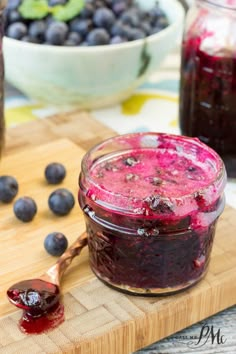 blueberry jam in a glass jar on a cutting board next to fresh blueberries