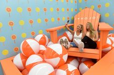 two women sitting in an orange and white chair with beach balls on the floor next to them