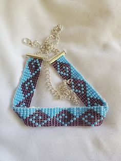 a blue and black beaded necklace on a white sheet with a chain hanging from it