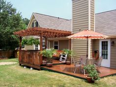 a deck with chairs and an umbrella in the yard next to a house on a sunny day