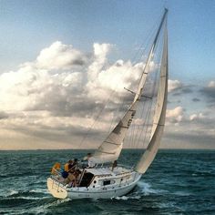 a sailboat with people on it sailing in the ocean under cloudy skies and clouds