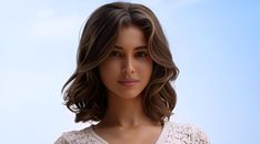 a woman with shoulder length brown hair is looking at the camera while wearing a white top