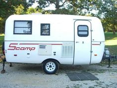 the camper is parked on gravel near trees