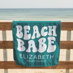 a beach towel hanging on a wooden fence near the water and sand at a beach