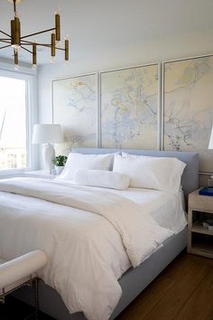 a bed with white sheets and pillows in a bedroom next to a large painting on the wall