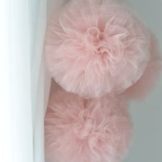 two fluffy pink pom poms hanging from the side of a white curtain