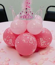 a table topped with pink balloons and a tiara on top of it's head