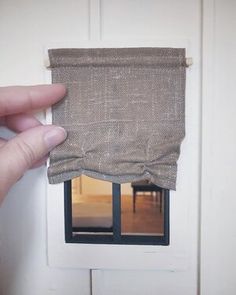 a hand is holding up a piece of burlocked fabric over a window