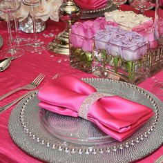 the table is set with silverware and pink napkins, roses in vases