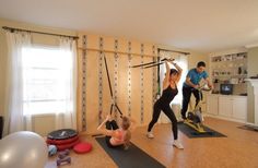 a man and woman doing exercises on exercise bikes in a living room with other people