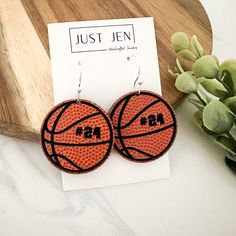 basketball earrings with the number 24 on them sitting next to a plant and a piece of wood