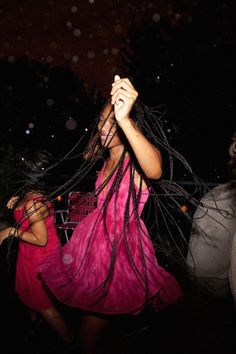 a woman in a pink dress is dancing with her hands on her head while another person holds the string attached to her hair