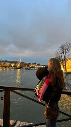 a woman is standing on a bridge looking at the water and buildings in the distance