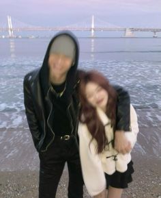 two people standing next to each other in front of the ocean and bridge behind them