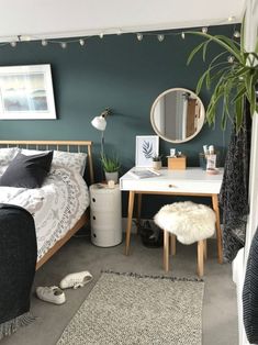 a bedroom with a bed, desk and mirror on the wall next to a potted plant