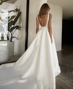 a woman in a white wedding dress is looking at her own reflection on the wall