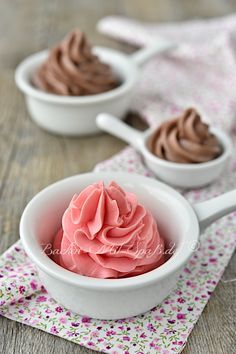 two white bowls filled with pink and brown frosting on top of a wooden table