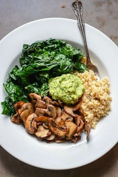 a white plate topped with mushrooms, spinach and couscouse next to a fork