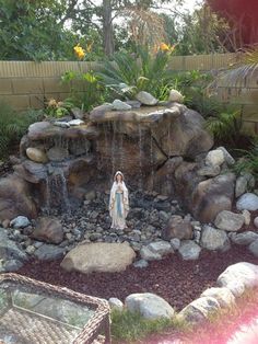 there is a small fountain in the middle of this garden with rocks and plants around it