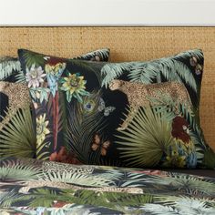 two pillows on top of a bed covered in jungle animals and plants with palm leaves