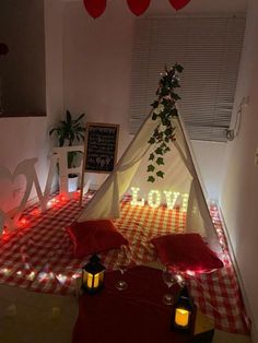 a teepee tent with lights on the floor and pillows in front of it that says love