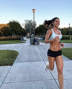 a woman running down a sidewalk in a white top and black shorts with her hair blowing back