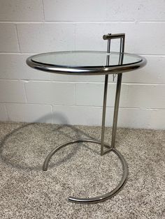 a glass and metal table on carpeted floor next to white brick wall in corner