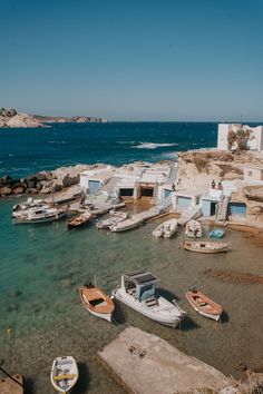 several small boats are docked in the water near some buildings and rocks on the shore