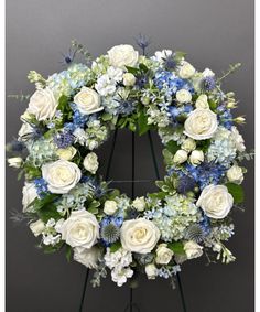 a wreath with white and blue flowers is displayed on a easel in front of a gray wall