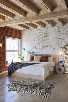 a bedroom with brick walls and exposed ceilings, white bedding, and rugs on the floor