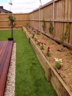 a garden with grass and flowers in the back yard, next to a wooden fence