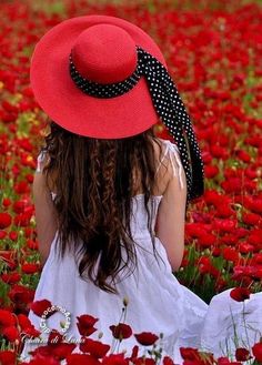 a woman in a red hat sitting in a field of flowers with her back to the camera