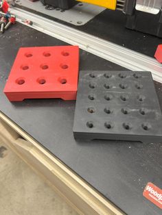 two red and black plastic blocks sitting on top of a workbench with tools