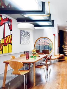 a dining room with wooden floors and art on the wall above it, along with modern furniture