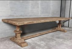 a large wooden table sitting in front of a white brick wall on concrete flooring