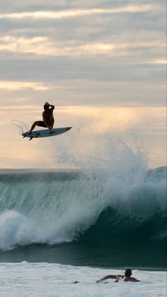 a man on a surfboard is in the air above a wave as another person swims nearby