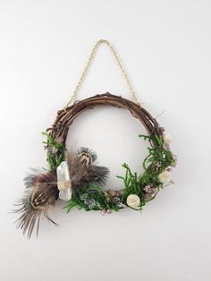 a wreath with flowers and feathers hanging on a chain