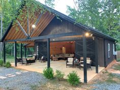 a covered patio area with chairs and tables in front of a barn style building surrounded by trees