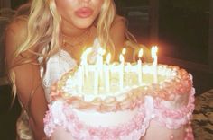 a blonde woman sitting in front of a cake with lit candles on it and looking at the camera