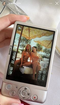 a person holding up a cell phone with two women on the screen and an umbrella in the background