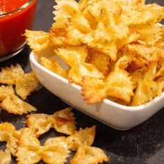 a white bowl filled with potato chips next to a red sauce