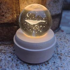 a glass ball with a whale on it sitting on top of a wooden stand next to a lamp