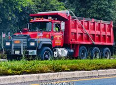 a large red dump truck parked on the side of the road next to some trees