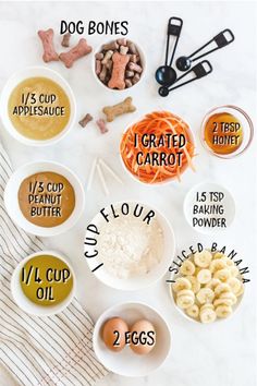 the ingredients for dog treats laid out in bowls on a white table with striped towel